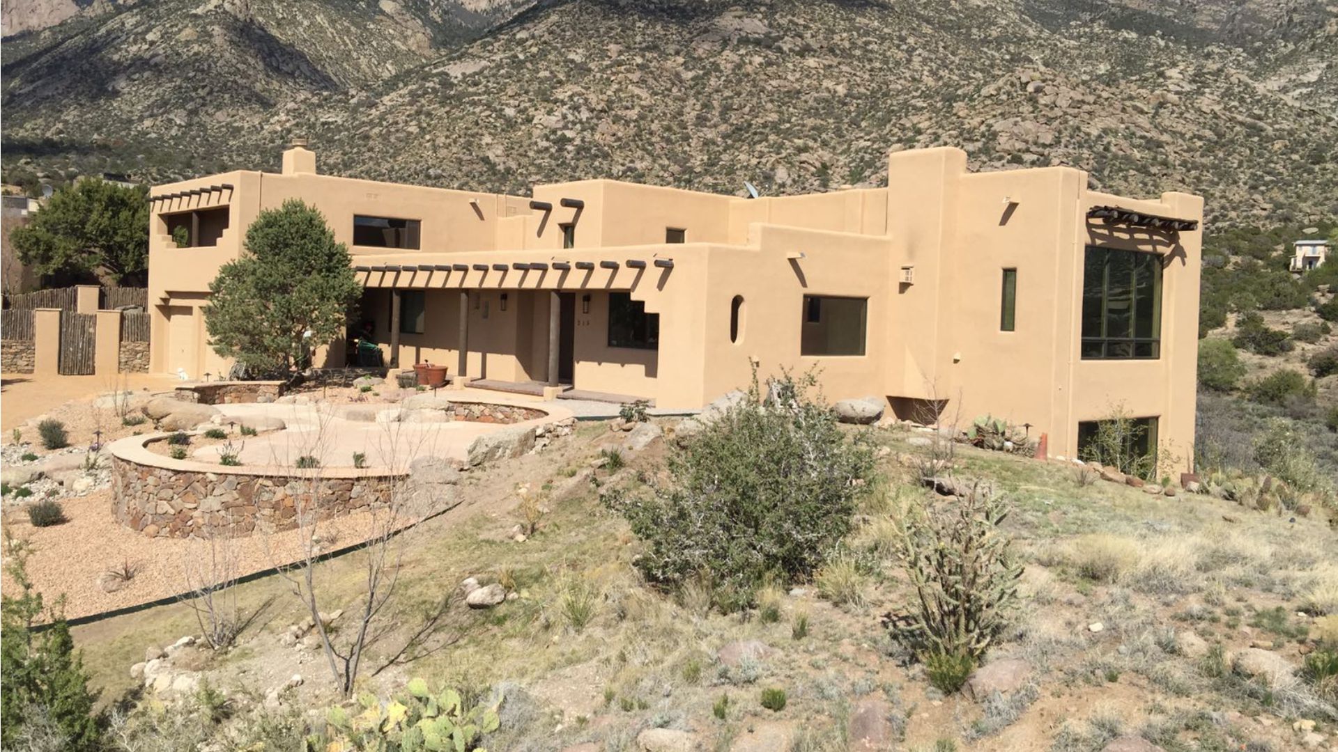 A large adobe house stands prominently with majestic mountains rising in the background, showcasing a serene landscape.