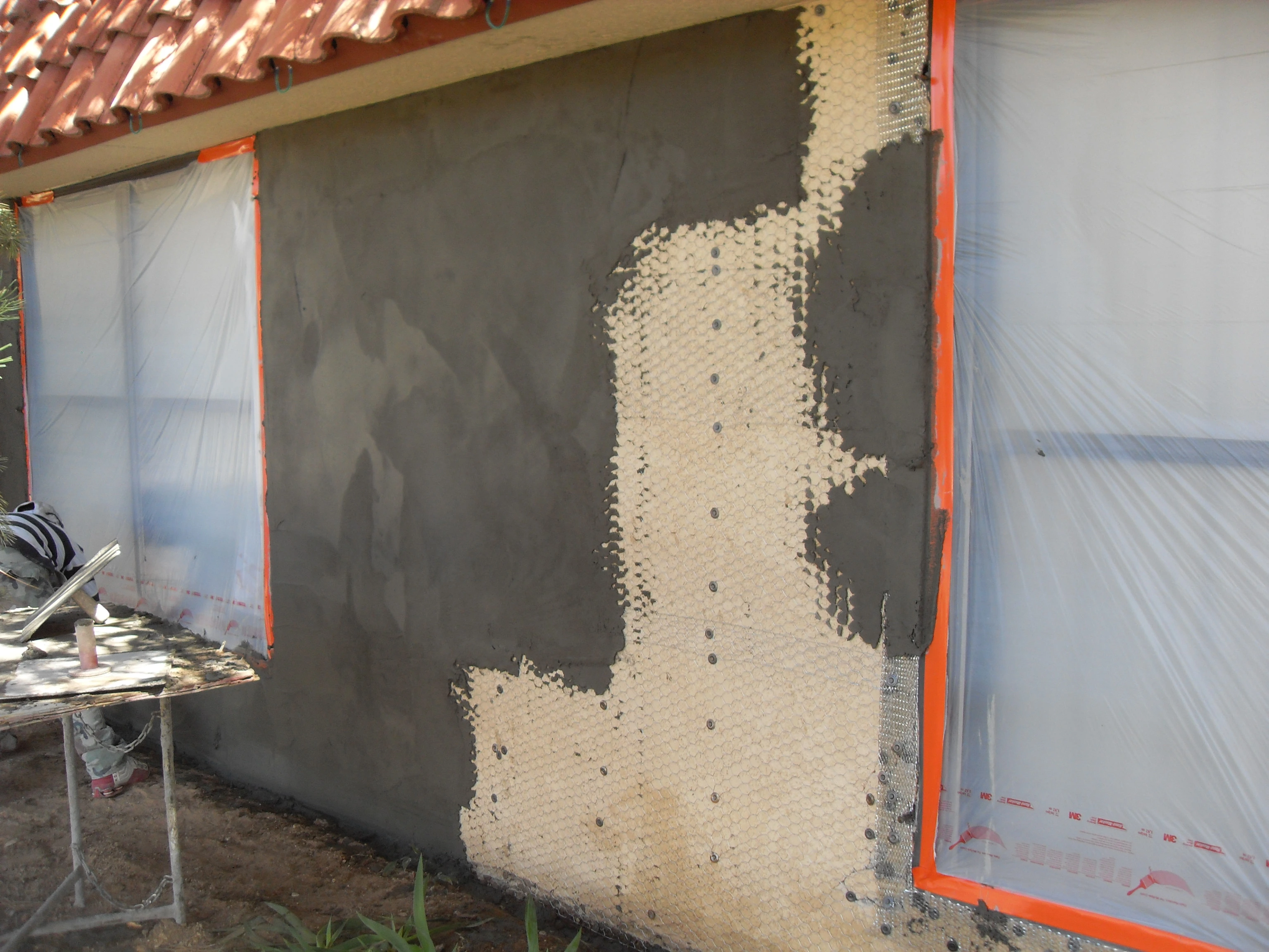 A man is engaged in home repairs, with a tarp draped over the house to safeguard it from the elements.