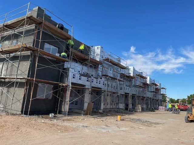 Construction workers diligently labor on a building site, surrounded by scaffolding and construction materials.