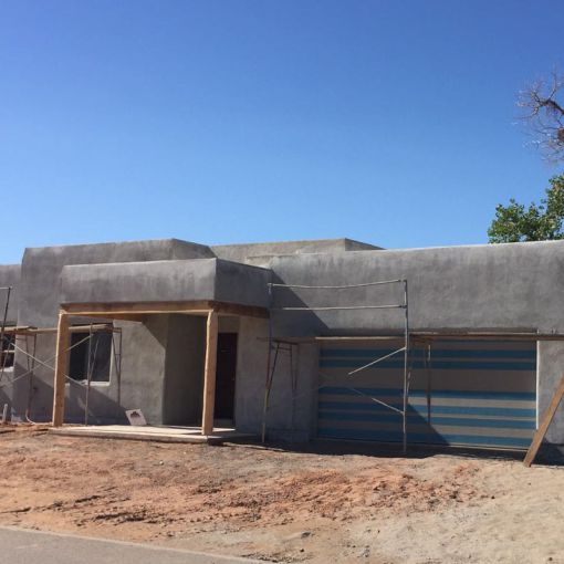 A construction site featuring a house under construction with concrete walls and blue paint being applied.